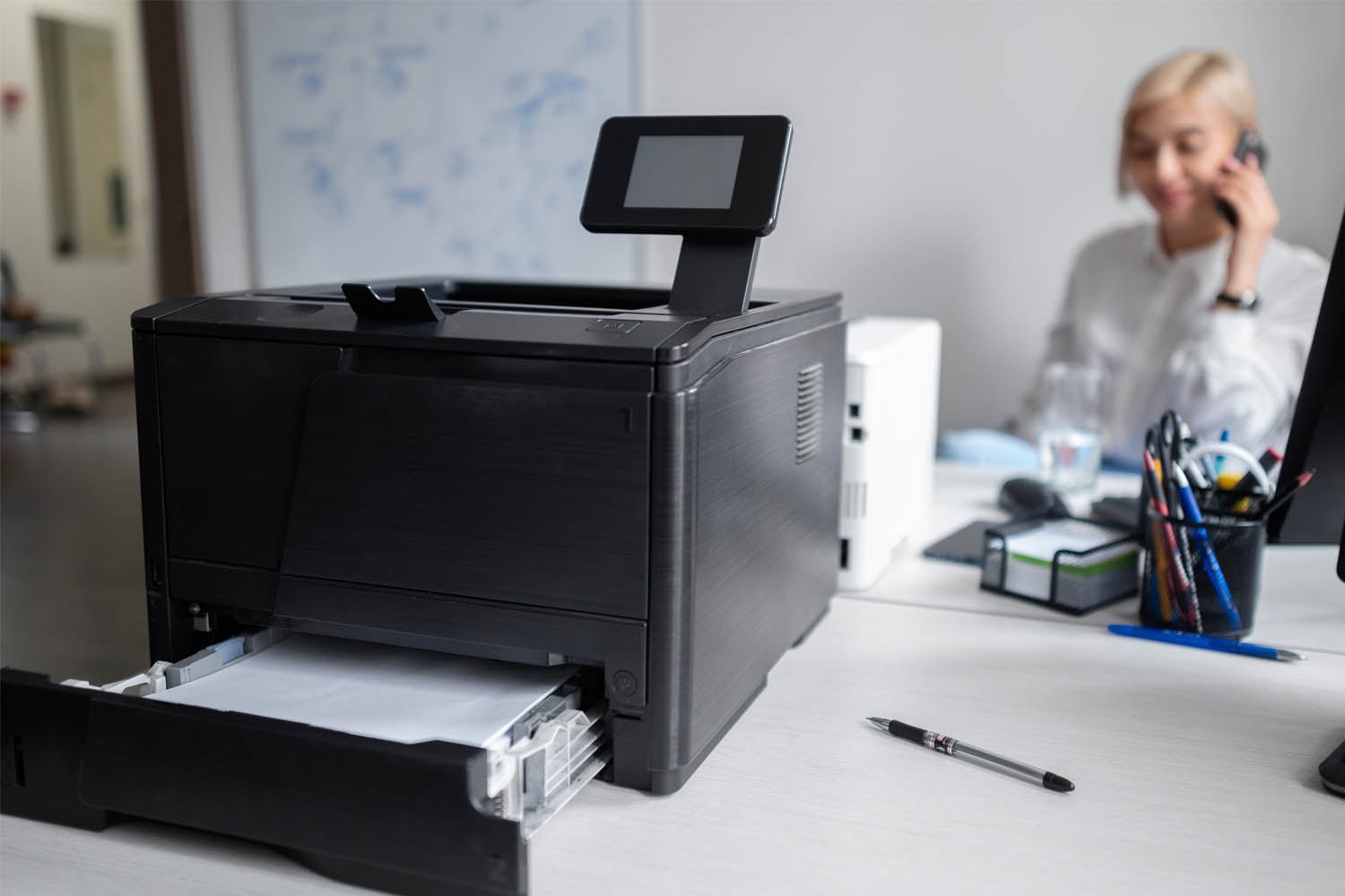 impressora epson ecotank em cima de mesa com mulher ao fundo falando ao telefone