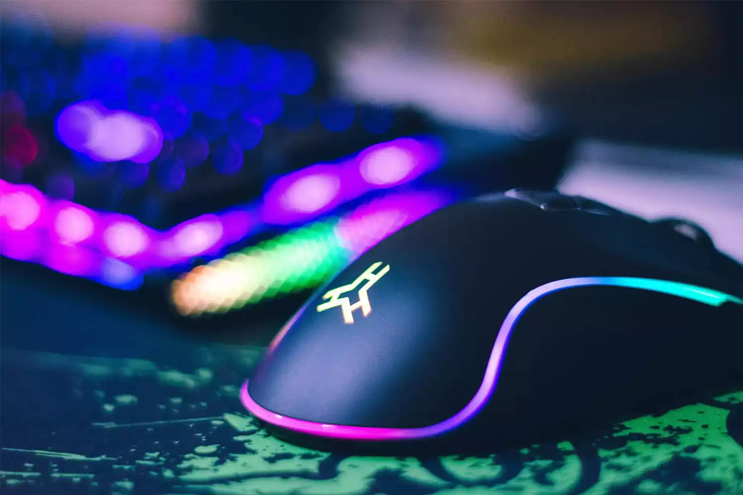 Mouse gamer ao lado de teclado sobre mousepad em cima de uma mesa