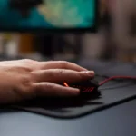 pessoa usando um mouse sobre um mousepad em cima de uma mesa de computador