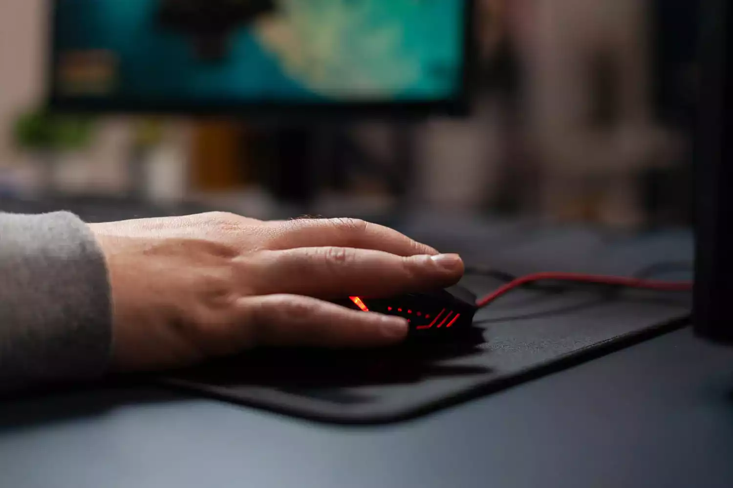 pessoa usando um mouse sobre um mousepad em cima de uma mesa de computador