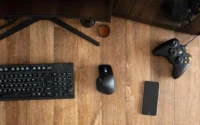 Teclado e mouse Dell ao lado de smartphone e controle de jogo em cima de uma mesa de madeira