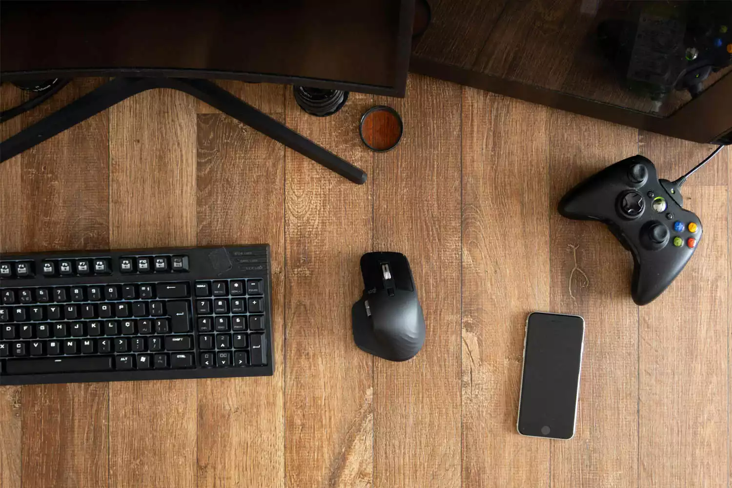 Teclado e mouse Dell ao lado de smartphone e controle de jogo em cima de uma mesa de madeira