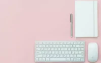 Teclado para escritório ao lado de mouse, caneta e caderno de notas sobre uma mesa com tampo rosa