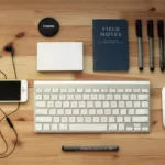 Teclado Para PC barato ao lado de mouse, smartphone, canetas e bloco de notas sobre uma mesa de madeira