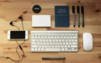 Teclado Para PC barato ao lado de mouse, smartphone, canetas e bloco de notas sobre uma mesa de madeira