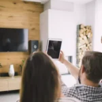 família sentada na sala com pai segurando tablet, mãe e filha ao lado em frente a uma tv smart 85 polegadas