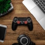 notebook gamer em promoção em cima de escrivaninha com controle, celular e fone de ouvido