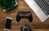 notebook gamer em promoção em cima de escrivaninha com controle, celular e fone de ouvido