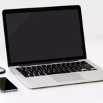 computador portatil em cima de uma mesa ao lado de maçã e celular