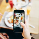 moça segurando um celular para tirar foto de um prato de comida ilustrando celular na Magazine Luiza