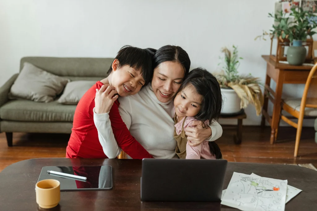 tablet-huion-kamvas-pro-13-capa mãe abraçando dois filhos menino e menina sentada em frente a uma mesa com tablet, computador e desenhos em cima