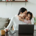 mãe abraçando filha enquanto usa tablet para desenho