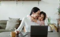 mãe abraçando filha enquanto usa tablet para desenho