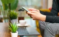 homem sentado em sofá em frente a mesinha com notebook segurando um celular ilustrando celular Motorola em Lançamento