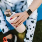 moça com roupa esportiva sentada com uma garrafa de água na mão e usando um smartwatch, ilustrando o smartwatch polar